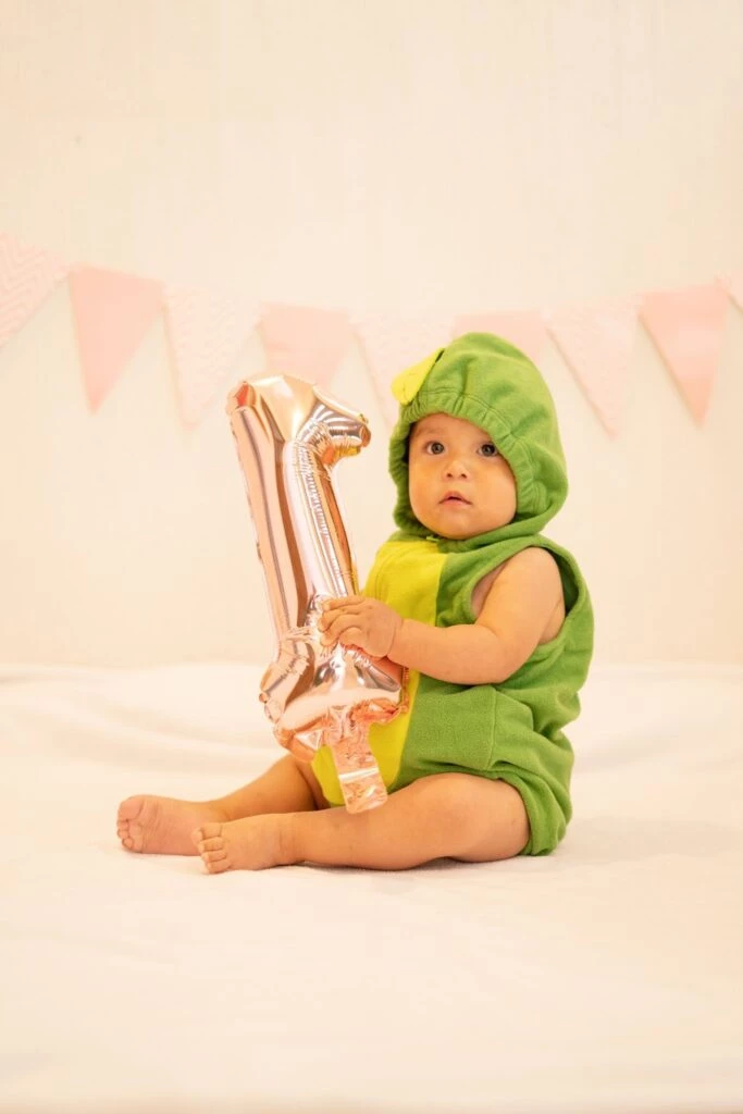 A baby in a green romper holding an inflatable balloon